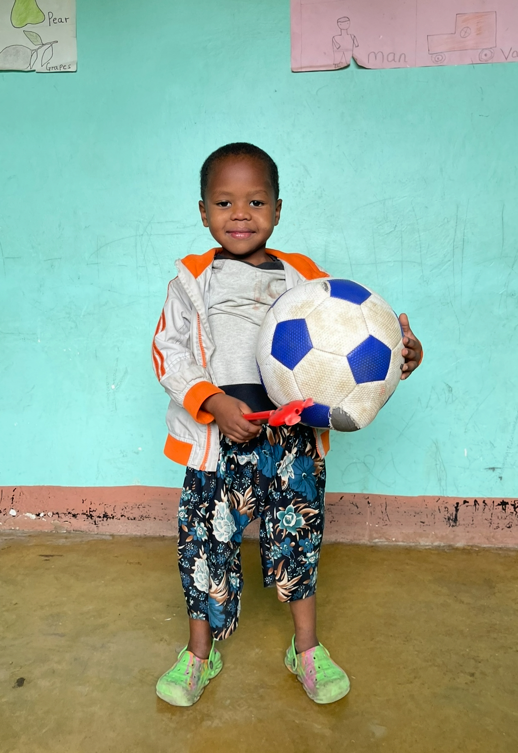 A child standing with a football and a toy in Arusha.