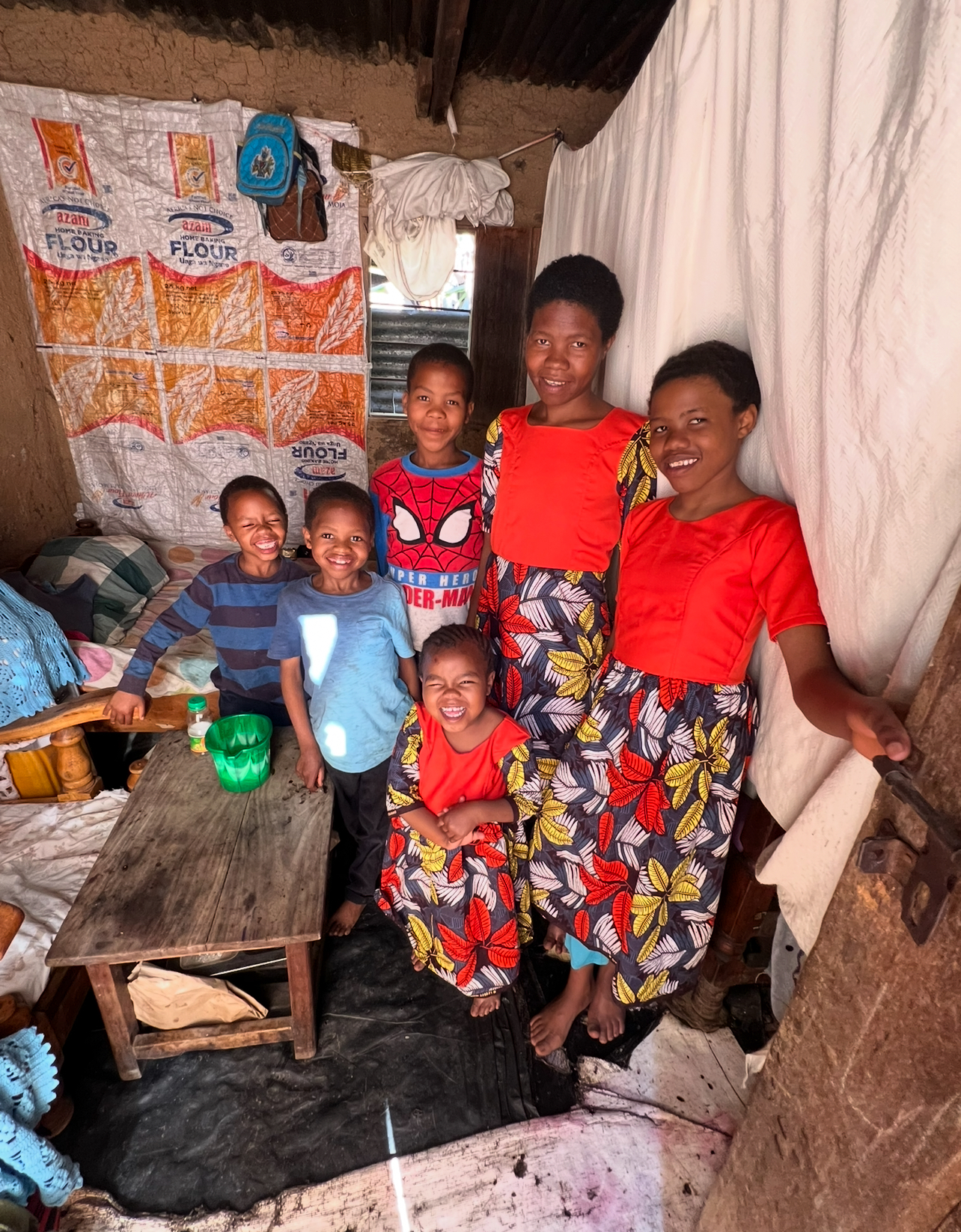 Six children and young people of one family standing together in their home, smiling at the camera.